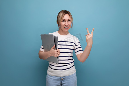 身穿休闲条纹毛衣、笔记本电脑在蓝色背景上显示两根手指的迷人女商人的水平照片