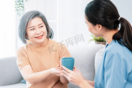 女性护理员为她心满意足的老年患者端上一杯咖啡。