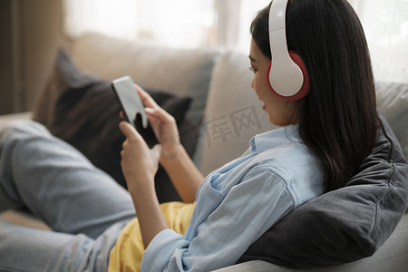 手机听音乐摄影照片_年轻女子在家里使用智能手机听音乐。