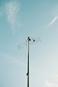 以干净的蓝天为背景的杆顶单警戒摄像机的极简主义照片