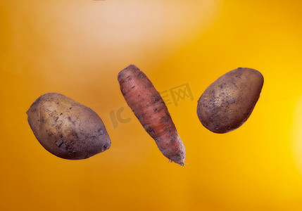 橙色背景上丑陋的土豆和胡萝卜。