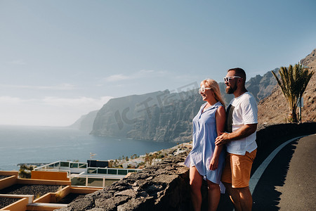 西班牙加那利群岛特内里费岛日落时分，一对热恋中的情侣站在观景台上，背景是 Acantilados de Los Gigantes 山脉