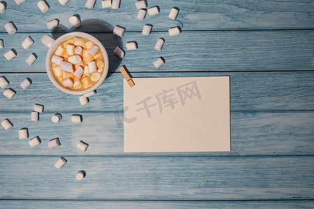 空的问候语或邀请卡模拟了白色的咖啡和棉花糖在木制的蓝色背景。