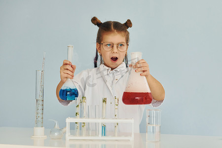 扮演了摄影照片_穿着外套的害怕的小女孩用设备在实验室里扮演科学家