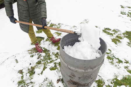 中年妇女正在用铲子在桶里收集雪，自然资源