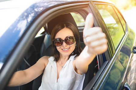一位戴着墨镜、长相潇洒的中年妇女把手伸出车窗外，竖起大拇指。