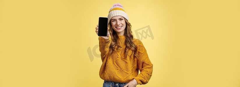 迷人外向的微笑时髦女孩伸出手臂，向您展示全新的智能手机，展示微笑满意的咨询朋友使用应用程序编辑照片手机、黄色背景放置的过滤器