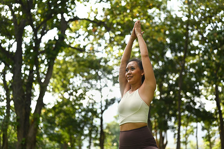 东风勇士摄影照片_积极的千禧一代女性练习瑜伽，站在勇士的姿势中，背景是自然环境
