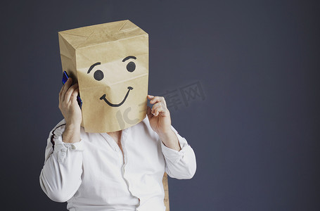 男笑脸摄影照片_性格开朗的男人头上顶着一个袋子，脸上带着拉长的笑脸。