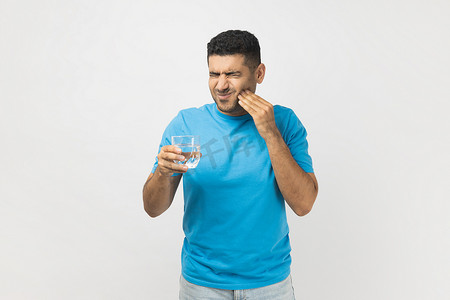 不刮胡子摄影照片_不健康、不刮胡子的男人拿着一杯冷水，感觉牙齿疼痛，牙齿敏感。