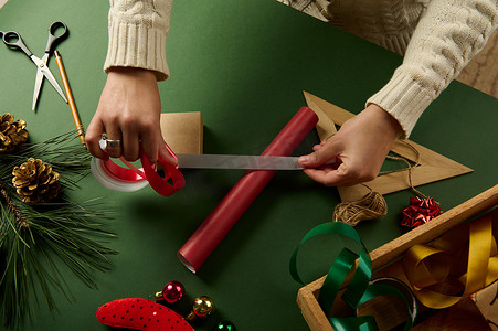端午节礼摄影照片_顶视图手拿着白色丝带在包装圣诞和新年礼物的红色包装纸上。
