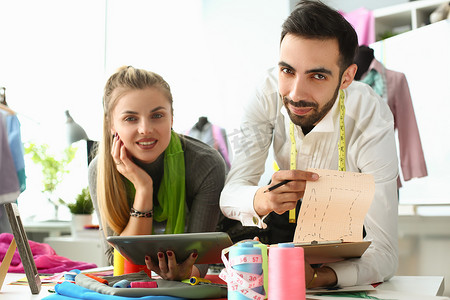 年轻女商人设计师女裁缝拿着平板电脑男同事展示衣服草图