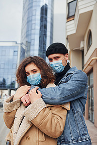 在检疫时间，一对戴着防护面具的夫妇在商业大楼附近的城市里互相拥抱。