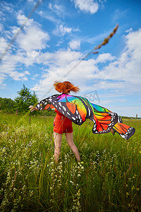 有红头发和蝴蝶翅膀的成年女孩在草地或草地上玩乐，在夏日阳光明媚的日子里花