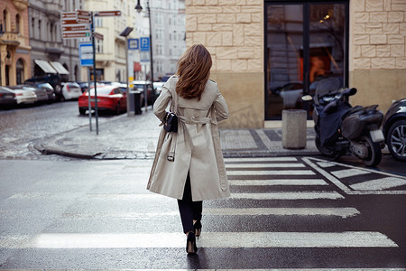 在城市建筑的背景下，穿着时髦服装的女性的背影穿过马路