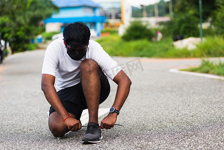 戴手表摄影照片_运动赛跑者黑人戴手表坐着他试着系着鞋带跑