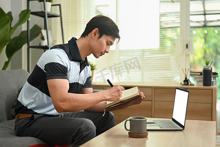 亚洲人做重要笔记的侧视图、计划日常约会和在客厅使用笔记本电脑的议程计划