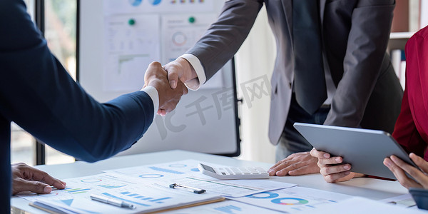 握手的商业领袖谈论图表，显示结果的财务图表正在分析和计算规划战略，商业成功建立过程