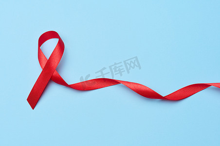 预防艾滋病病毒摄影照片_蓝色背景中突显出一条蝴蝶结状的丝红丝带，这是抗击艾滋病的象征，也是团结和支持的象征
