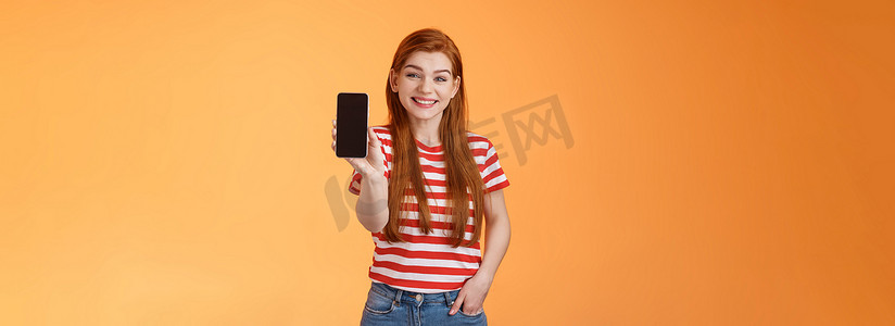 手机推广摄影照片_开朗帅气的 20 多岁红发女性介绍社交媒体特色产品手持智能手机、展示相机手机显示屏、推广设备应用、广泛微笑、橙色背景