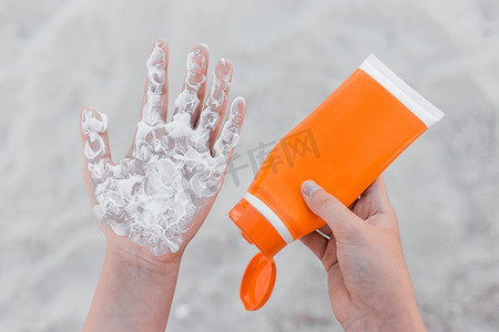 女孩手里拿着防晒霜，把它挤在手臂手掌上，以保护她免受沙滩背景下的阳光照射