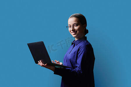 蓝色背景中使用笔记本电脑的少女高中生