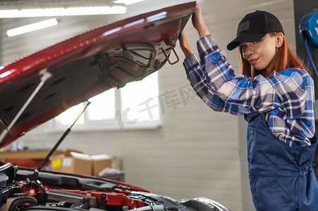 女汽车修理工在汽车服务中打开汽车引擎盖。