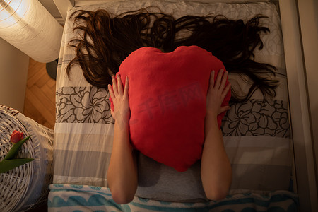 发出嘶嘶声摄影照片_这个女孩用一个红色的心形枕头盖住她的脸。