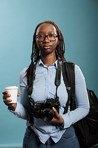 年轻的摄影爱好者在蓝色背景下享用饮料时拥有摄影设备。