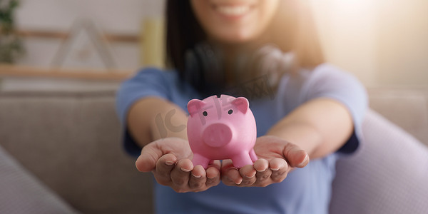 年轻的亚洲女人手把硬币放在粉红色的存钱罐里，以便账户省钱。