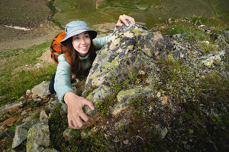 快乐的女人在户外徒步时爬上一块岩石。