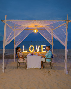 男女喝摄影照片_泰国普吉岛海滩上的浪漫晚餐，一对男女在海滩上共进晚餐