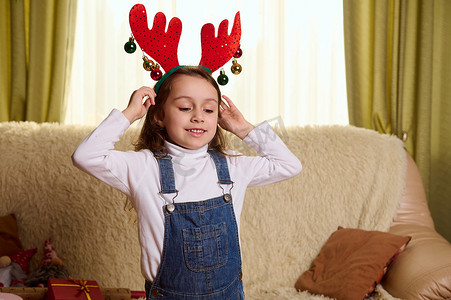 可爱的孩子，一个小女孩戴上鹿角鹿圈，在家里享受圣诞气氛。