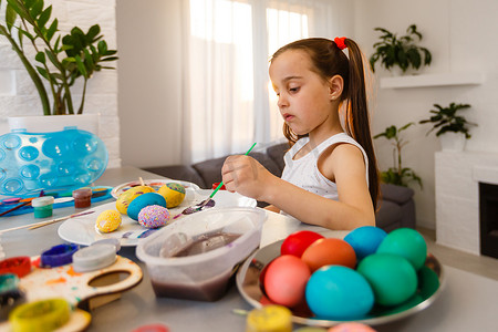 可爱的小女孩用刷子画鸡蛋。