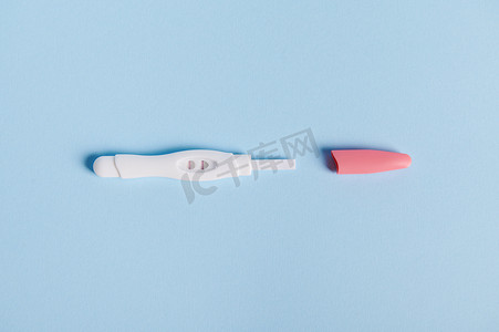 蓝色柔和背景上带有两条带的阳性妊娠试验试剂盒的孤立镜头。
