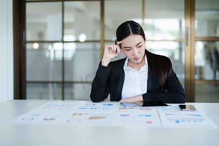 一张美丽的亚洲女员工的肖像，她在办公桌上使用财务文件时表情紧张