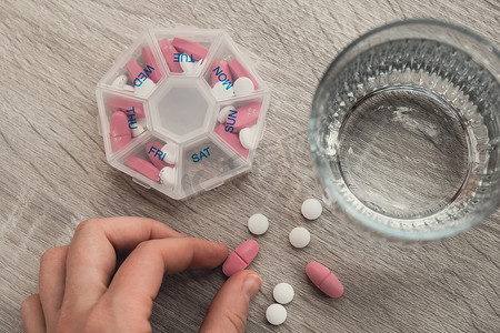 妇女分拣药丸组织者每周拍摄药丸盒特写镜头，每天服用药片剂量，用白色粉红色药物和胶囊服药。