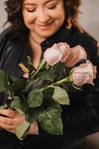 一位穿着黑色皮衣的时尚成年女性站着，室内有一束粉红玫瑰