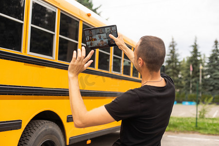 教师数字教育摄影照片_男教师或学生在校车附近使用数字平板电脑。