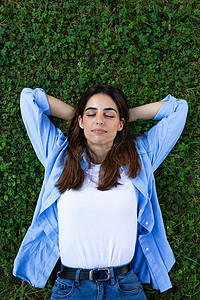 宁静、放松的年轻黑发女子闭着眼睛躺在草地上的垂直肖像。