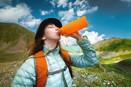 运动型白人女游客在青山中喝水瓶。