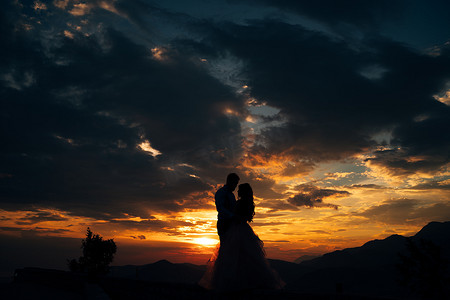 在洛夫森山上拥抱的新娘和新郎的剪影，在日落时俯瞰科托尔湾