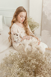 山羊女孩摄影照片_一个长头发的金发女孩坐在沙发上，家里有一只山羊。