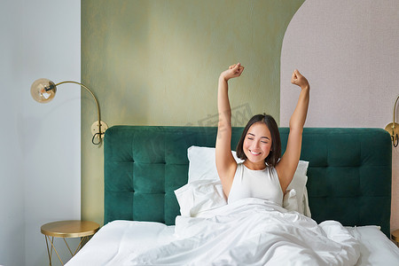 梦想早安摄影照片_微笑快乐的亚洲女孩的画像，醒来时充满热情，举起双手，在卧室里享受早安