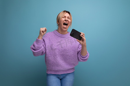 身穿紫色连帽衫、精力充沛的金发年轻女性顾问手持带模型的智能手机，在蓝色背景中唱歌，带复制空间