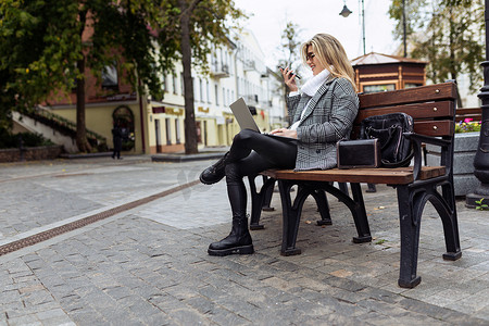 公园里坐在长椅上、膝上放着笔记本电脑的成熟女商人通过视频连线讲话