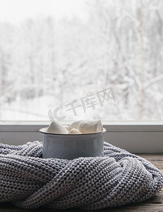 复古窗台上的咖啡配棉花糖和舒适的灰色毛衣，映衬着外面的雪景。