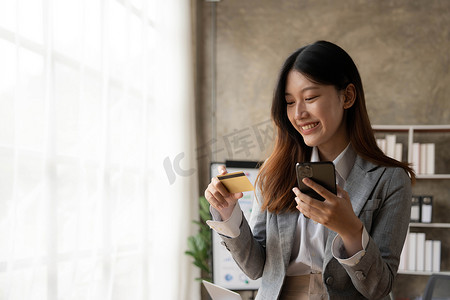 快乐的亚洲女商人在办公室使用手机在线支付。