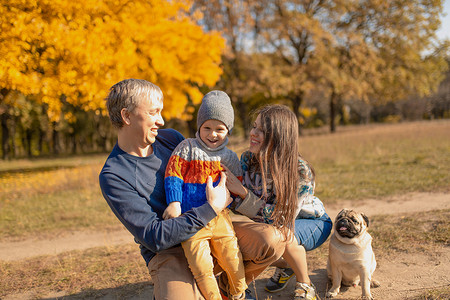 散步的小孩摄影照片_一个有小孩和狗的年轻家庭一起在秋季公园散步