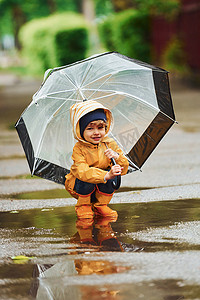 防水雨伞摄影照片_雨后穿着黄色防水斗篷、靴子和雨伞在户外玩耍的孩子
